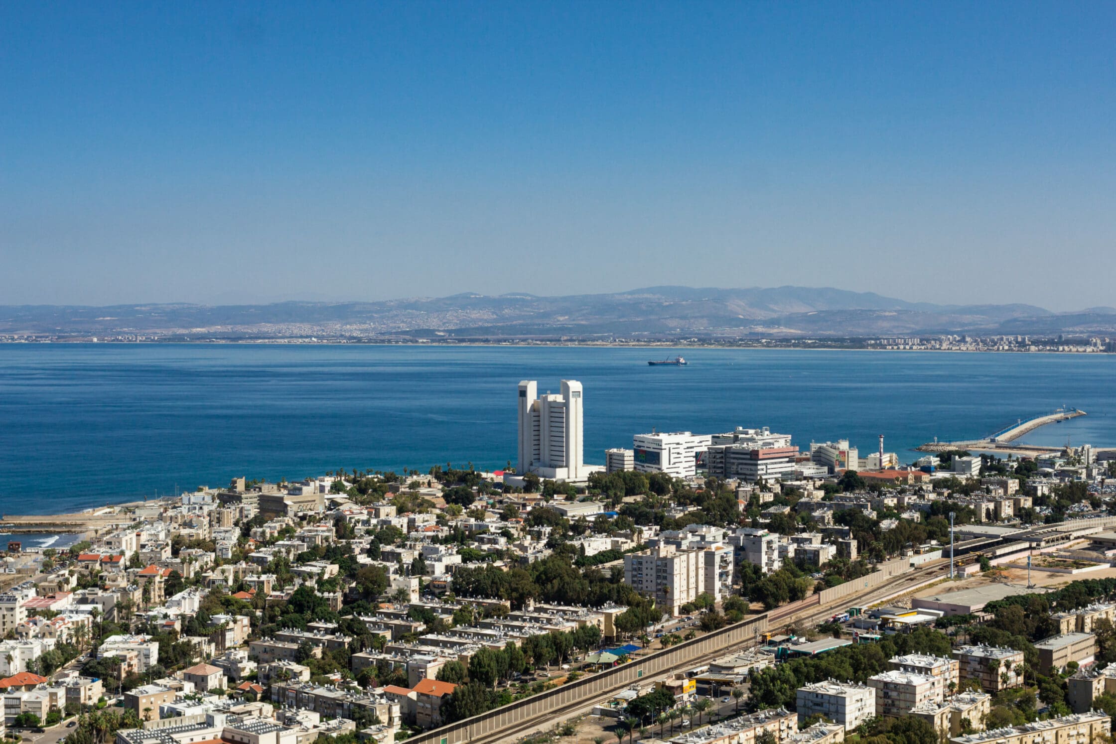 Blick auf die Hafeneinfahrt von Haifa, im Vordergrund ein Wohnviertel, im Hintergrund die hügelige Küstenlandschaft