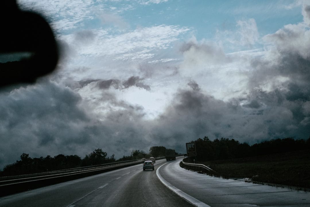 Blick aus der Frontscheibe eines Autos auf die Autobahn den Berg hinauf. Über der Autobahn bricht die Sonne durch die Wolken.