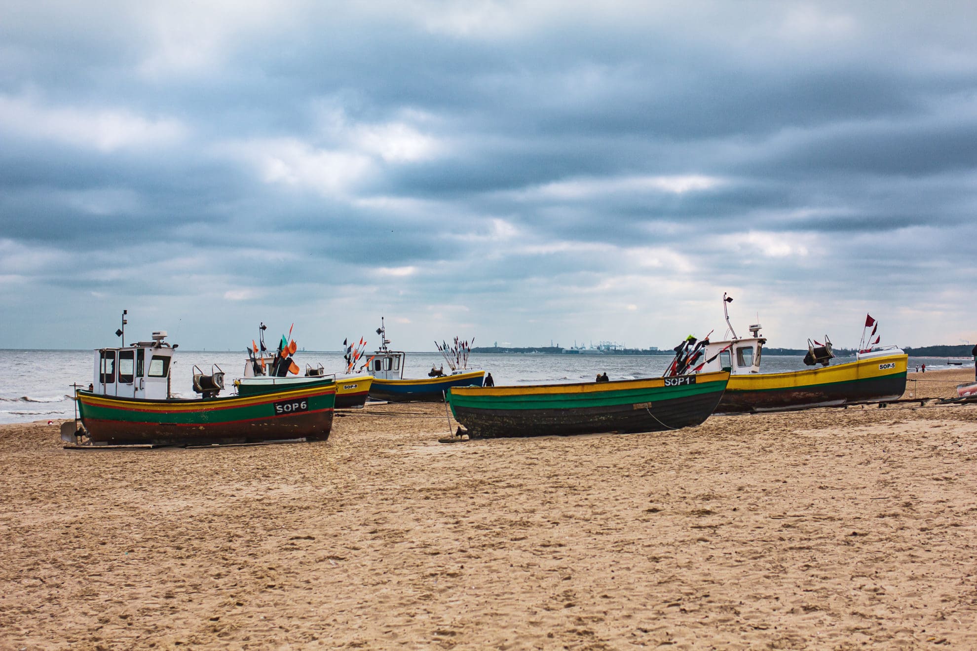 Mehrere kleine bunte Fischerboote liegen am Strand, über ihnen stehen dunkle Wolken.