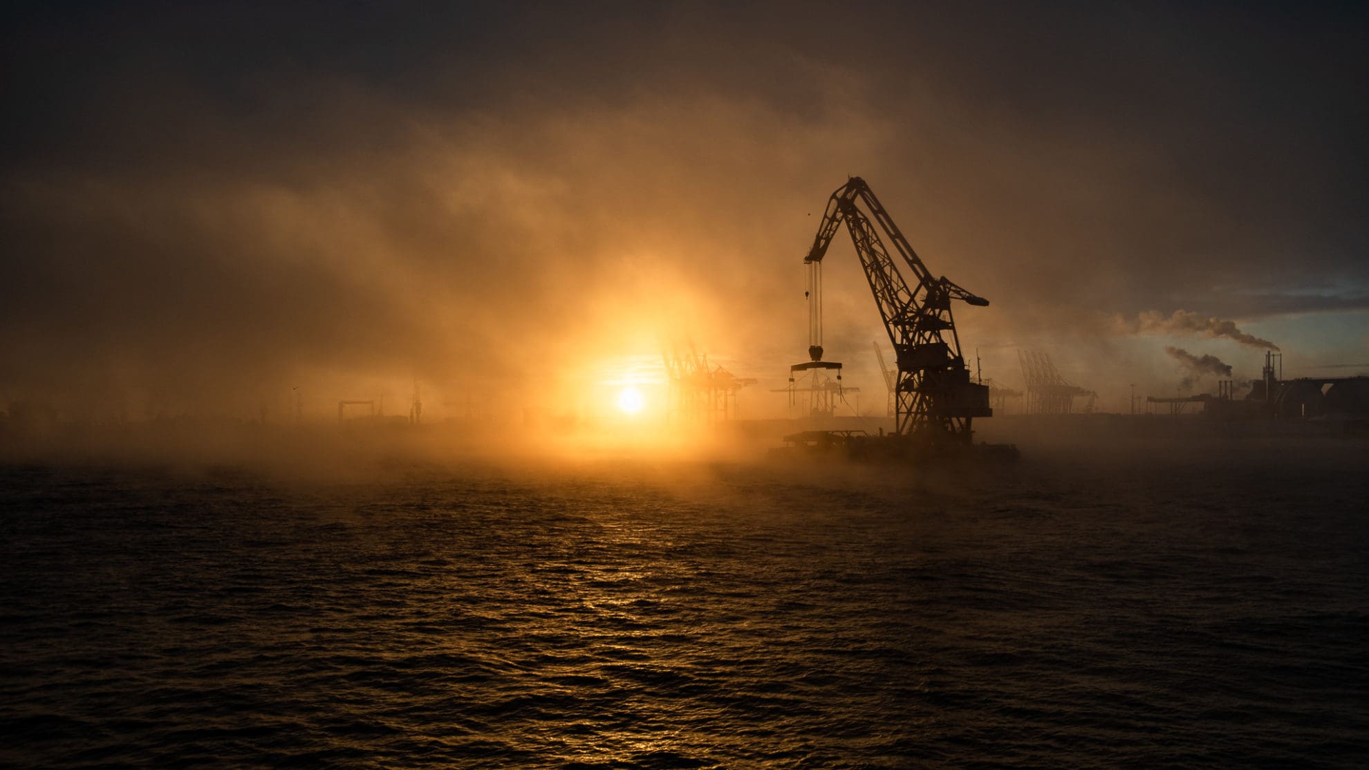 Im hellen Gegenlicht der Sonne schwimmt ein Schwimmkran über die Elbe durch feine Nebelschwaden.