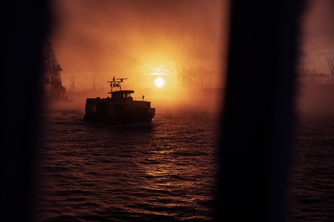 Im Gegenlicht der aufgehenden Sonne fährt eine Hafenfähre über die Elbe