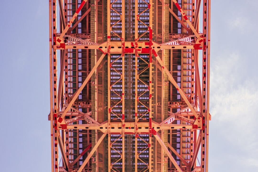 Rote Stahlkonstruktion einer Hängebrücke von unten fotografiert.
