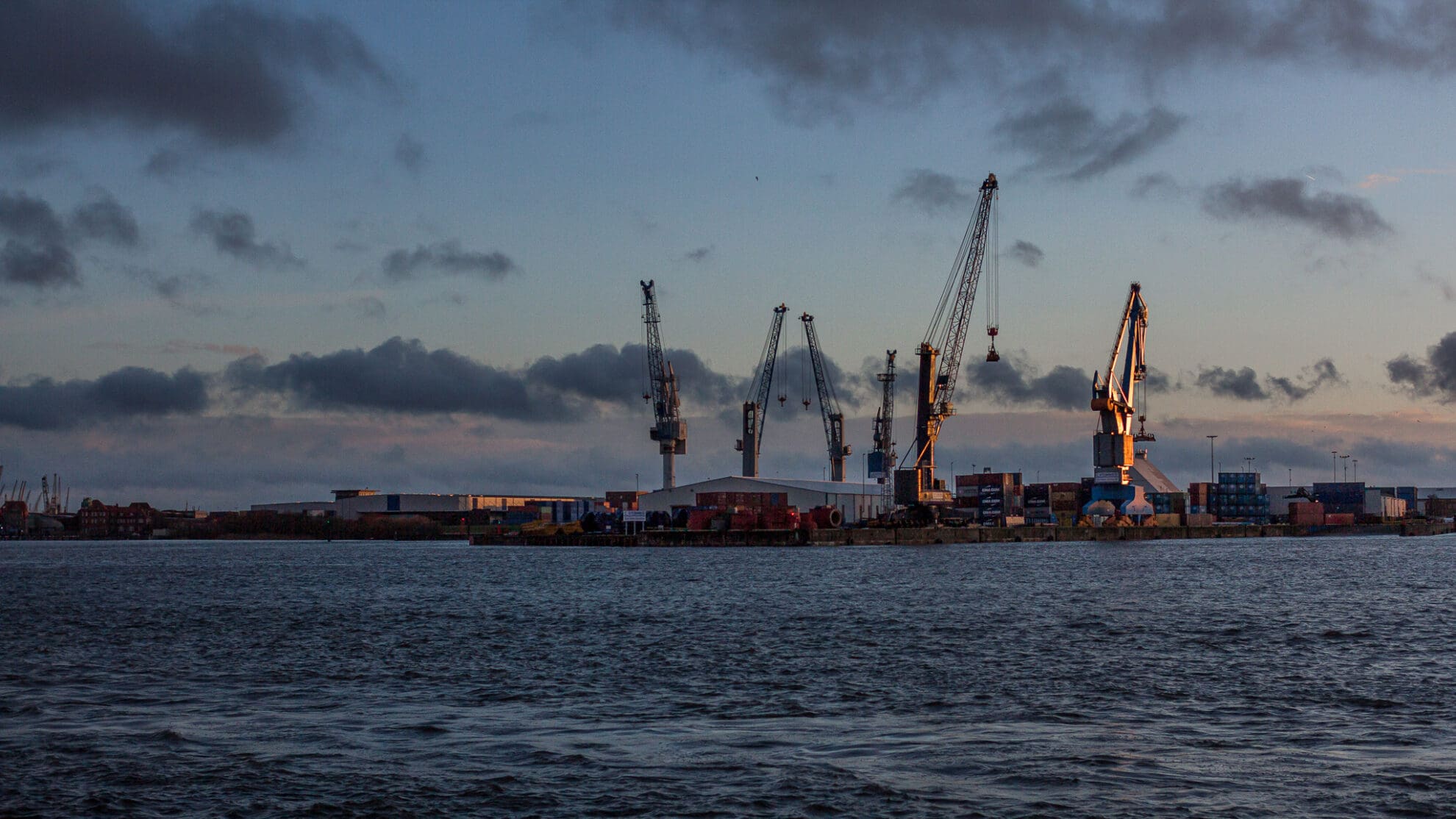 Sechs Kräne stehen im Licht der untergehenden Sonne im Hafen