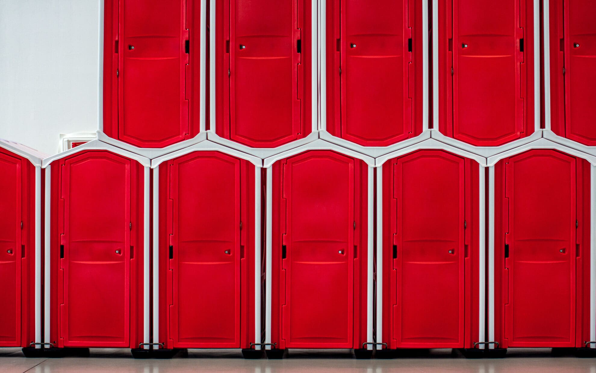Leuchtend Rote mobile Toilettenhäuschen stehen aneinandergereiht und aufeinander gestapelt.