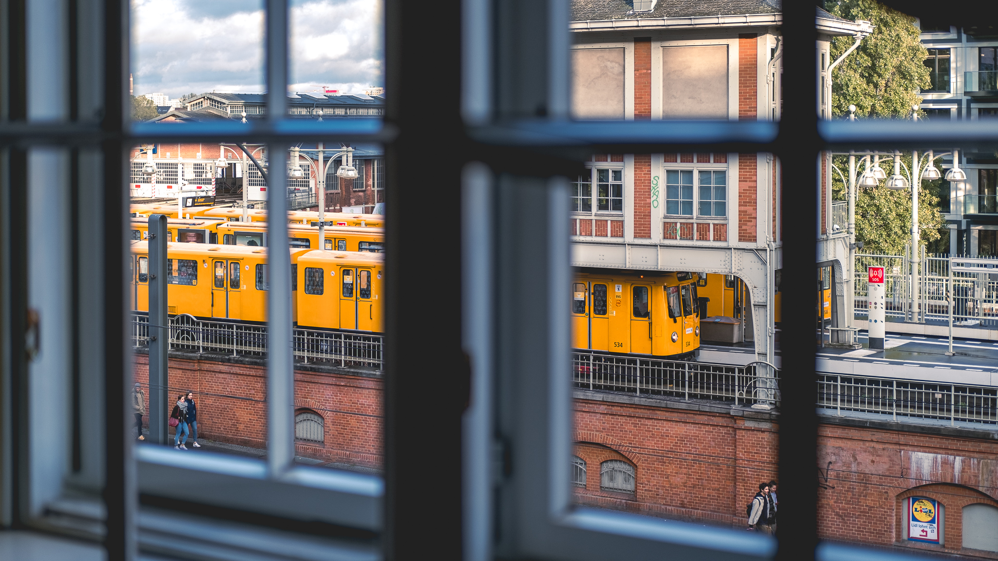 Eine gelbe Berliner U-Bahn, betrachtet durch ein Sprossenfenster, wartet am Bahnsteig auf die Weiterfahrt.