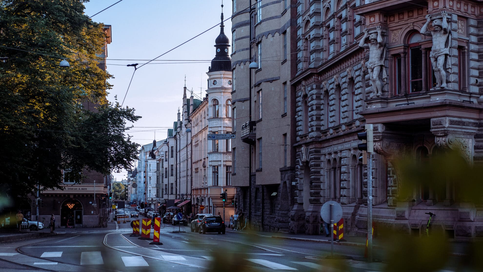 Blick über eine Straßenkreuzung in eine lange Straße, gesäumt von alten Gebäude mit verzierten Giebeln in der Abendsonne.