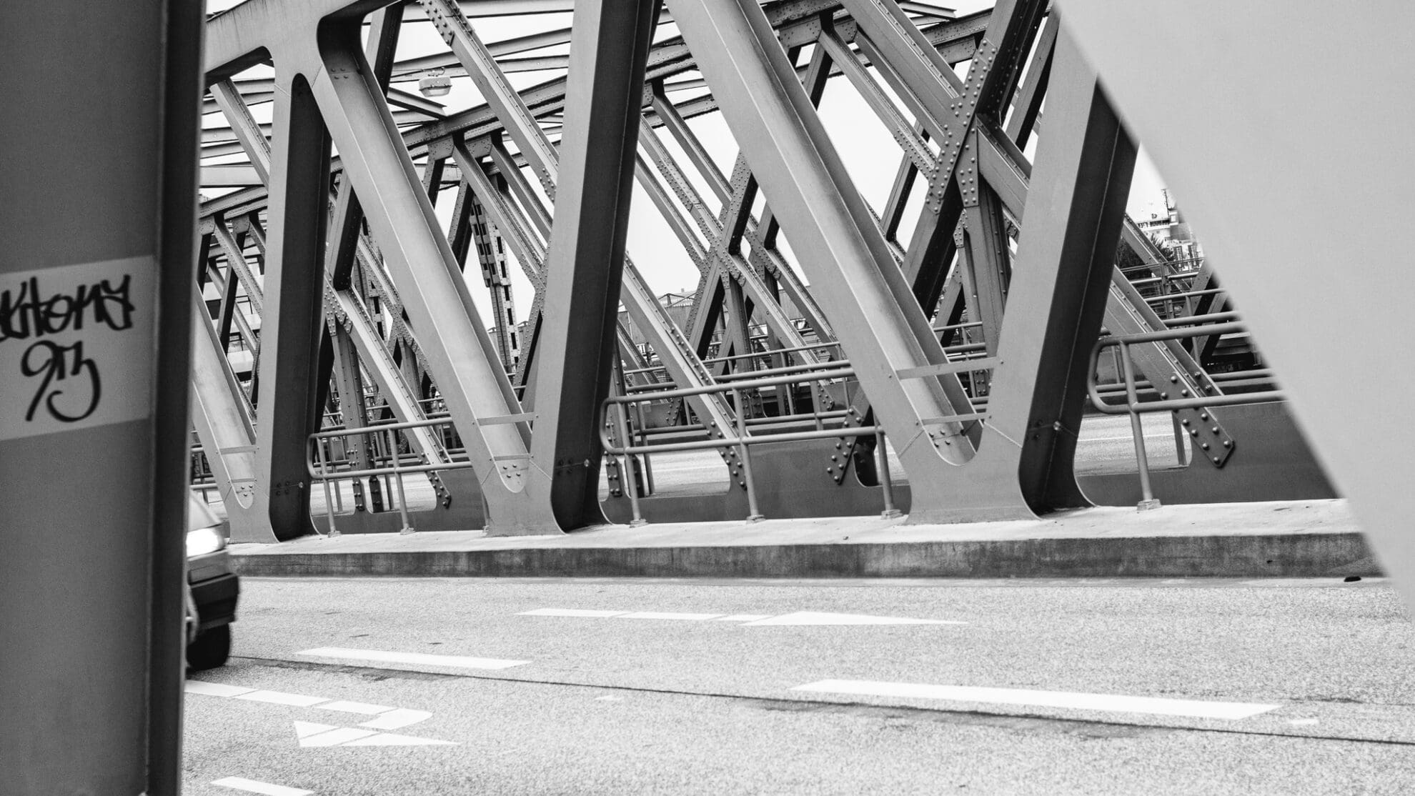 Schwarz-weiß Aufnahme durch die Querstreben einer Brücke mit Blick auf die dahinterliegende Brückenstreben